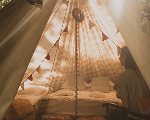 Interior of a clamping tent from outside of the tent looking in. There is a young female adult sitting in a chair while relaxing in the tent.