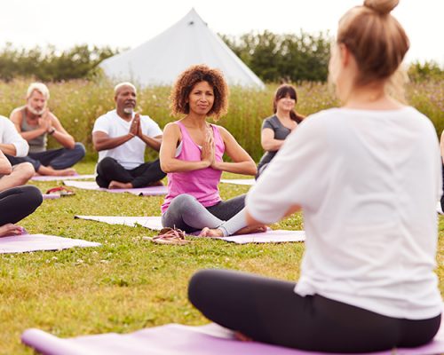 Female Teacher Leading Group Of Mature Men And Women In Class At Outdoor Yoga Retreat