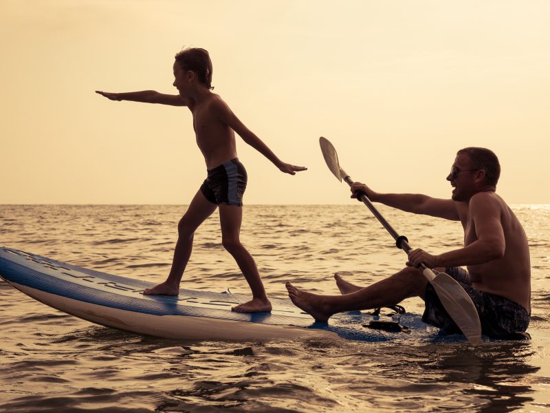 Father and baby son playing on the beach at the day time. People having fun outdoors. Concept of summer vacation and friendly family.