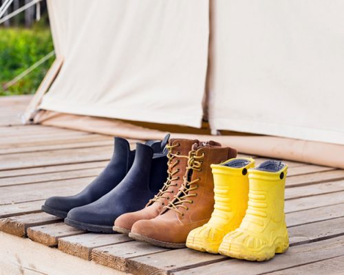 Three pair of shoes near canvas bell tent. Family trip concept